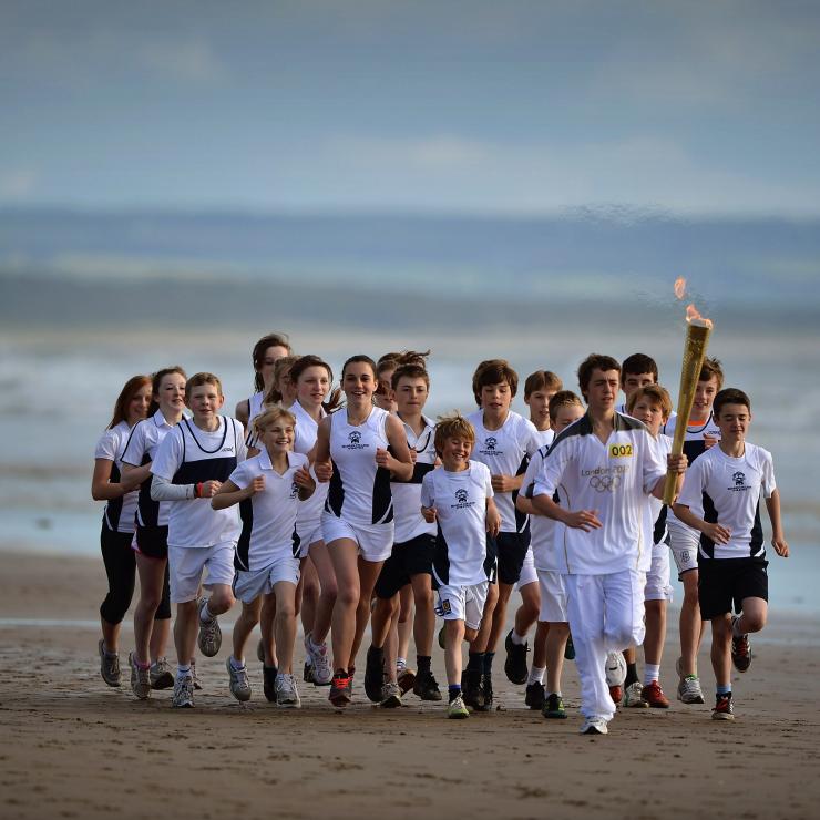 Un groupe d'enfant courent avec la torche olympique sur la plage