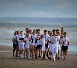 Un groupe d'enfant courent avec la torche olympique sur la plage